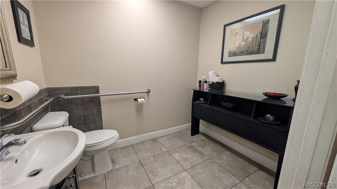 Bathroom with a pedestal sink, toilet, grab bars, and black console table.