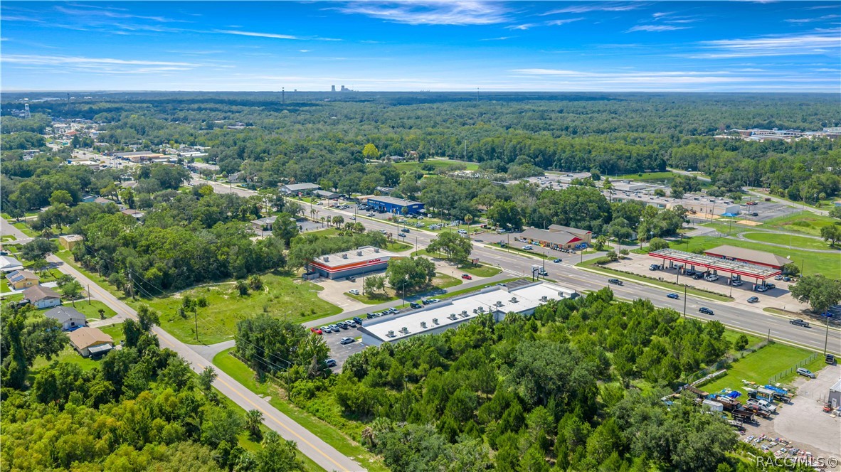 Aerial view of a wooded commercial area with roadside businesses, parking lots, and intersecting streets.
