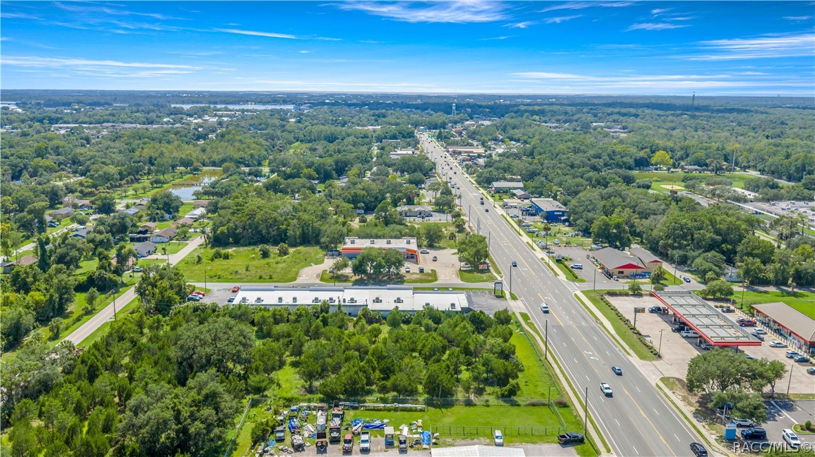 Aerial view of a tree-lined area and commercial buildings along a wide multi-lane road.
