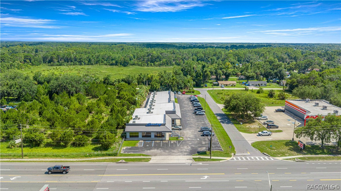Aerial view of a commercial building and parking lot beside a multi-lane road, with an Arby's nearby.