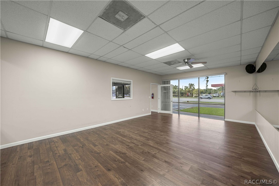Vacant commercial interior with wood-look flooring and large storefront windows facing the street.