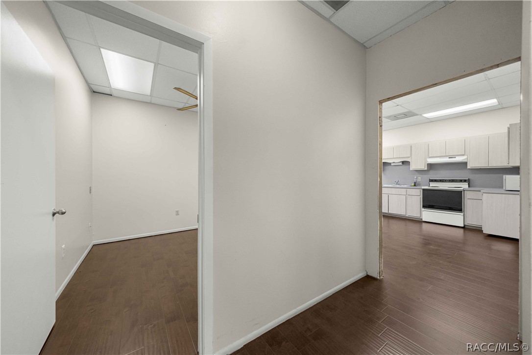 Vacant interior with dark flooring and an open doorway to a kitchen with light cabinets.