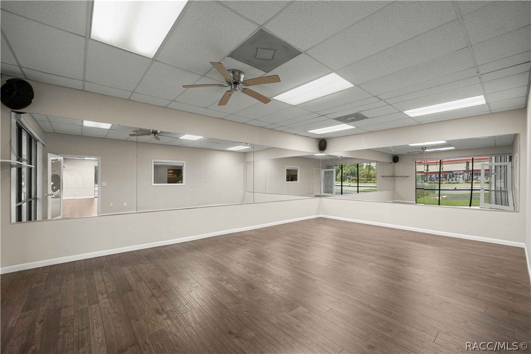 Vacant commercial interior with a mirrored wall, wood-look flooring, and storefront windows.