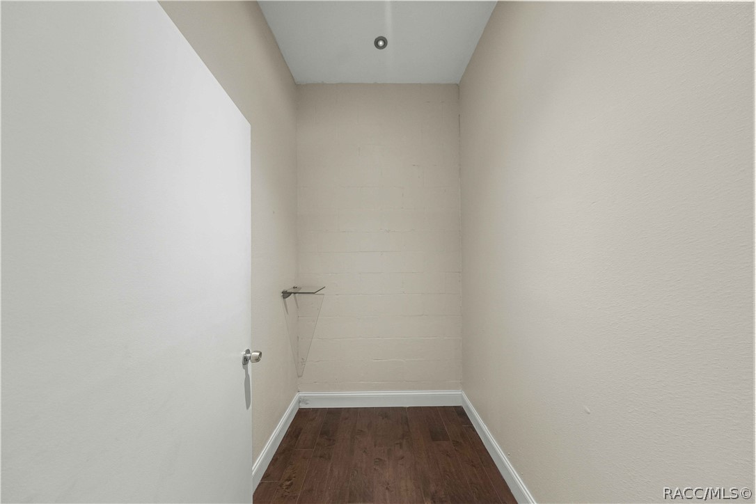 Empty narrow room with dark wood flooring, cream walls, and a small wall shelf.