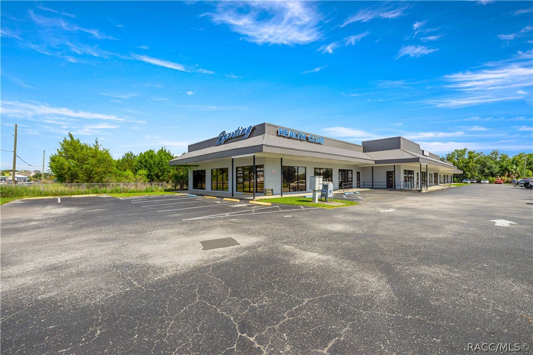 Single-story health club with a wide roofline and a large asphalt parking lot.