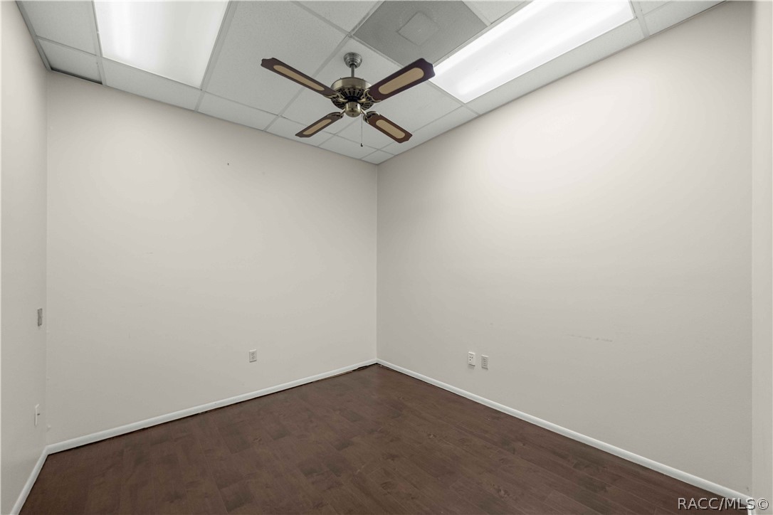 Empty room with dark flooring, white walls, and a ceiling fan.