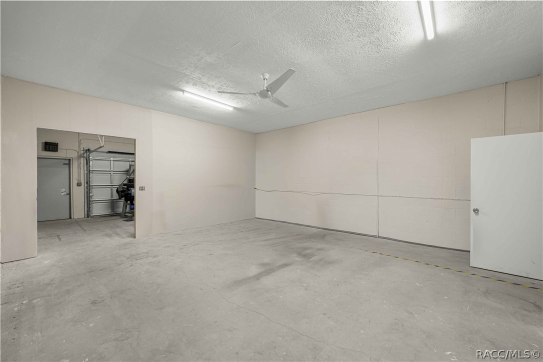 Vacant concrete-floored room with pale block walls, a ceiling fan, and an open passage to a roll-up door.