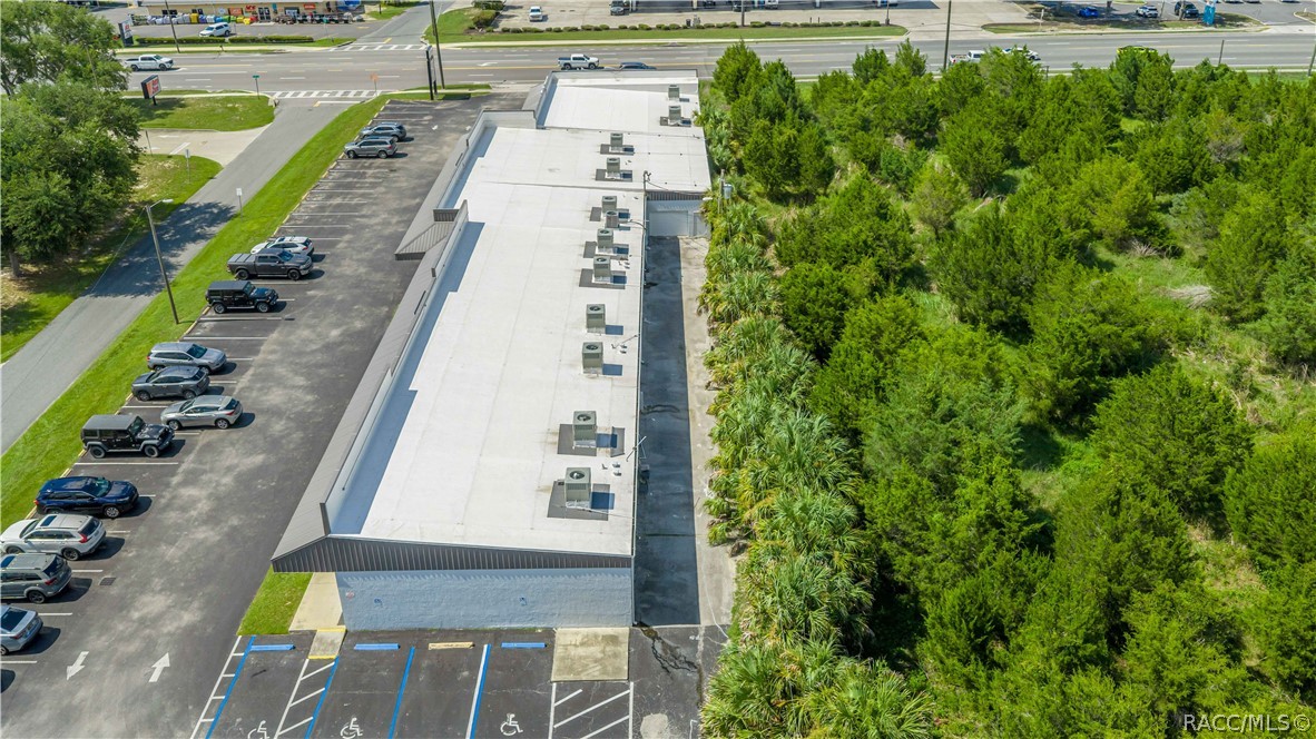 Aerial view of a commercial building, parking lot, and wooded land.