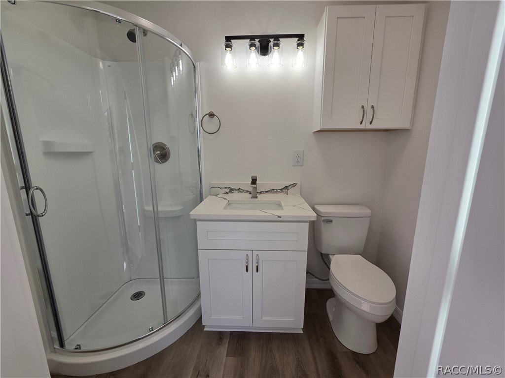 Bathroom with a curved glass shower, white vanity, wall cabinet, and toilet.