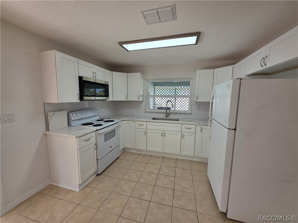 Kitchen with white cabinets, electric range, microwave, and beige tile flooring.