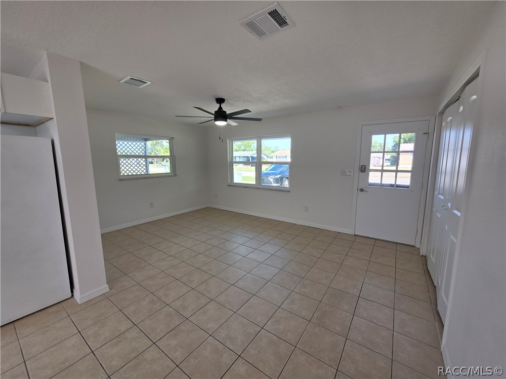 Empty kitchen with beige tile flooring, a black ceiling fan, windows, and a glass-paneled exterior door.