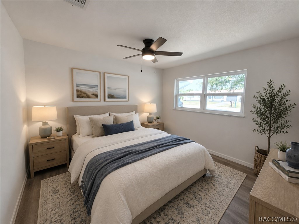 Staged bedroom with a white bed, blue throw, coastal prints, and a ceiling fan.