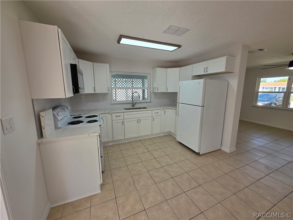 White kitchen with tiled floors, electric range, refrigerator, and lattice-covered sink window.