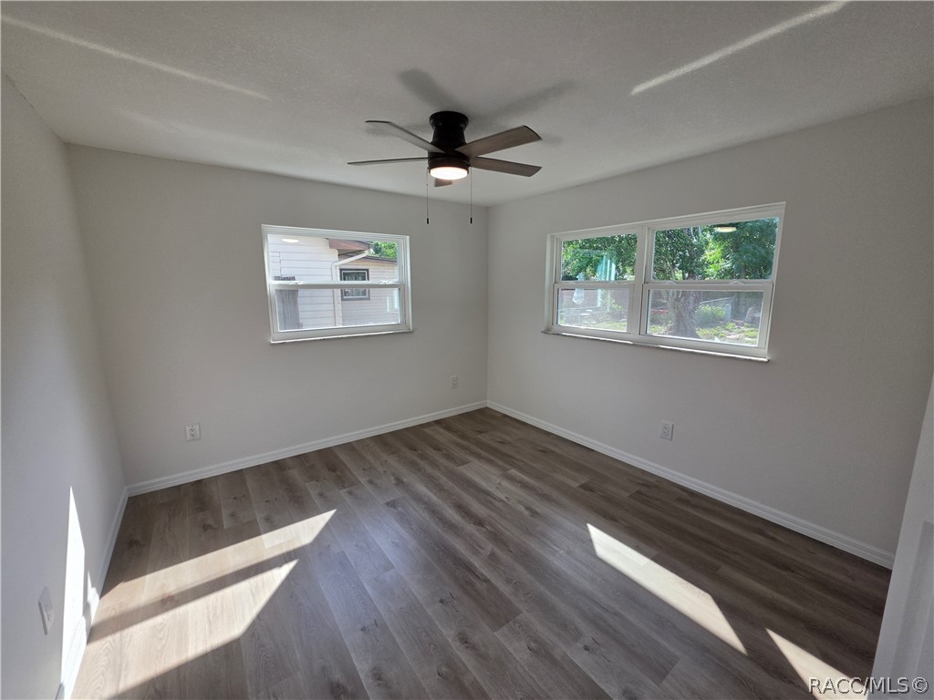 Vacant room with wood-look flooring, a ceiling fan, and two windows.
