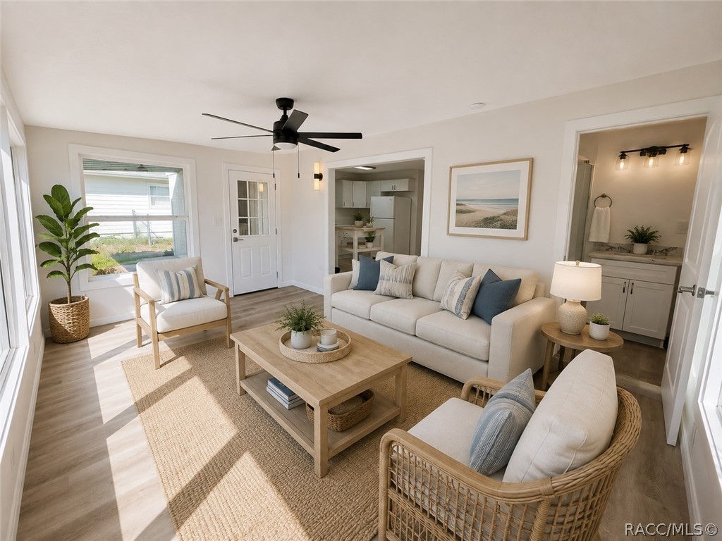 Staged living room with cream seating, a woven rug, ceiling fan, and open views into the kitchen and bathroom.