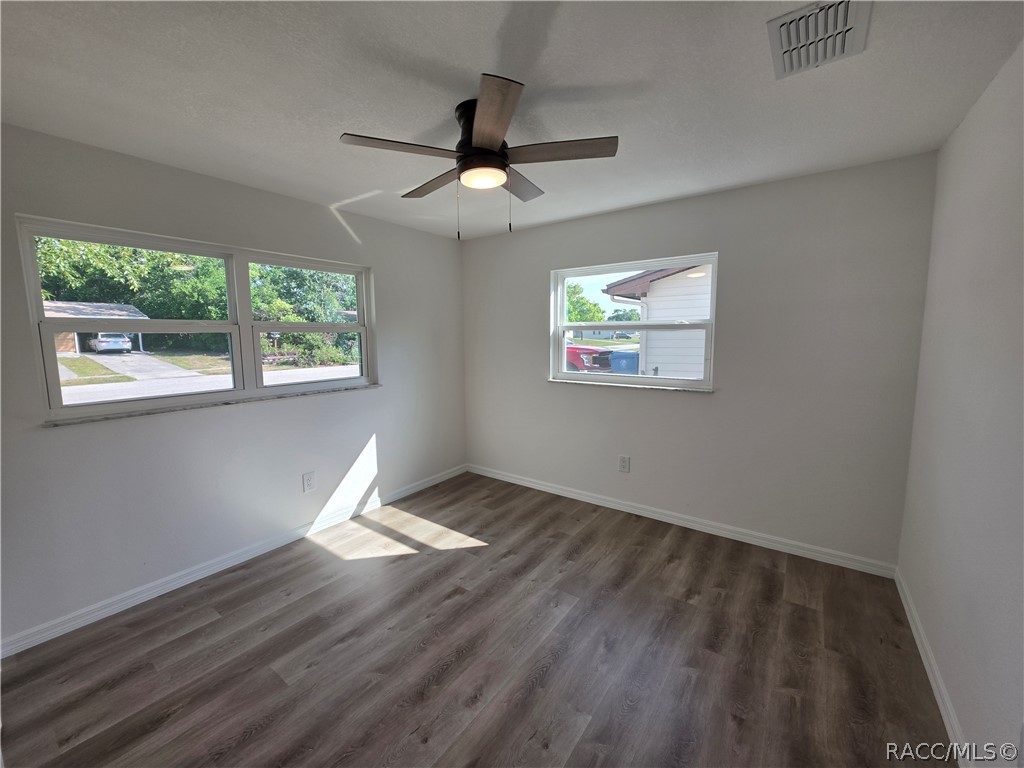Empty room with wood-look flooring, a ceiling fan, and three windows.