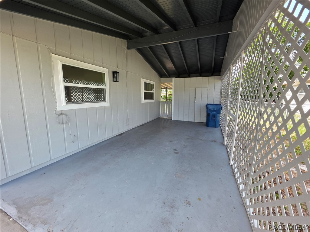 Covered concrete patio with white lattice sides and a dark exposed-beam roof.