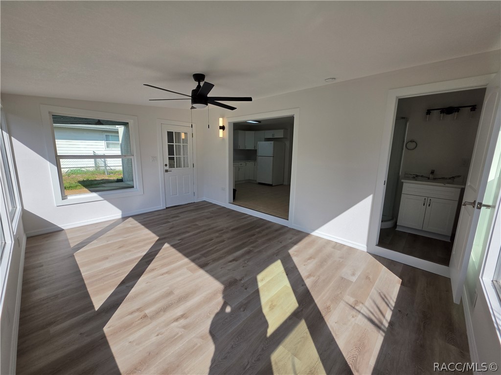 Unfurnished living room with wood-look floors, black ceiling fan, and views into the kitchen and bathroom.