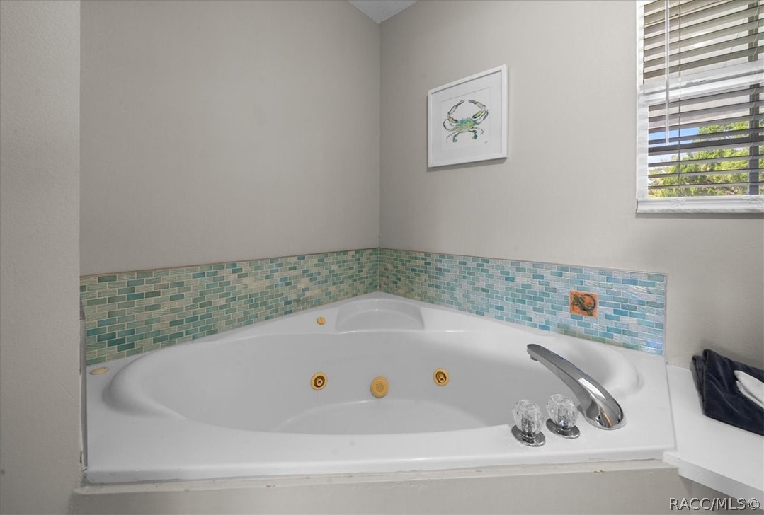 Corner jetted bathtub with blue-green mosaic tile backsplash and framed crab print.