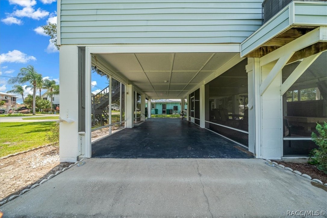 Covered carport beneath a light-colored house, with a concrete driveway and screened windows.