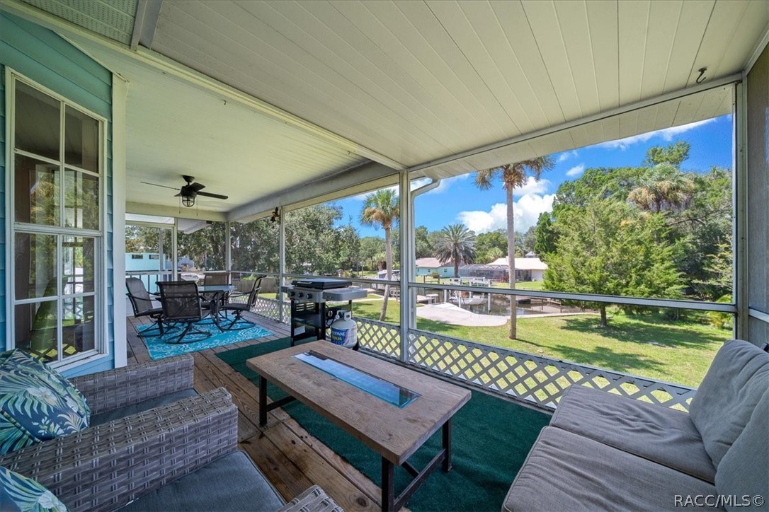 Covered patio with wicker seating and a grill overlooking a grassy yard and water.
