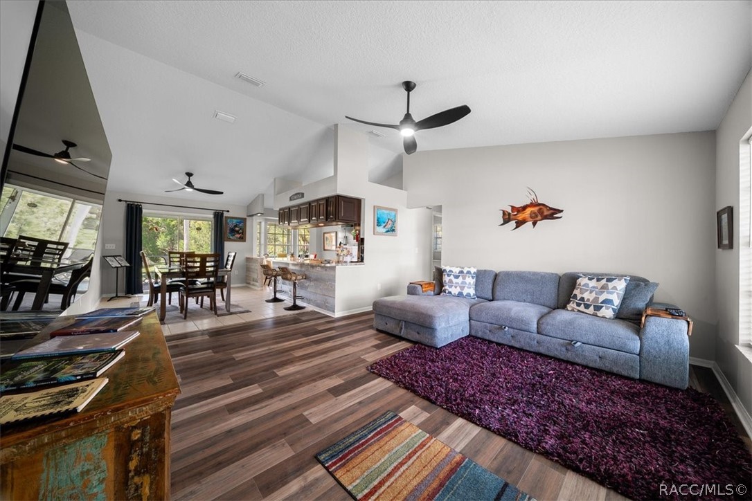 Open-plan living room with a blue sectional sofa, wood-look floors, and dining area.