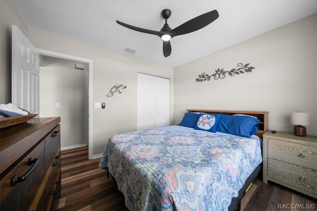 Bedroom with a large bed in a patterned quilt, blue pillows, and dark wood-look flooring.
