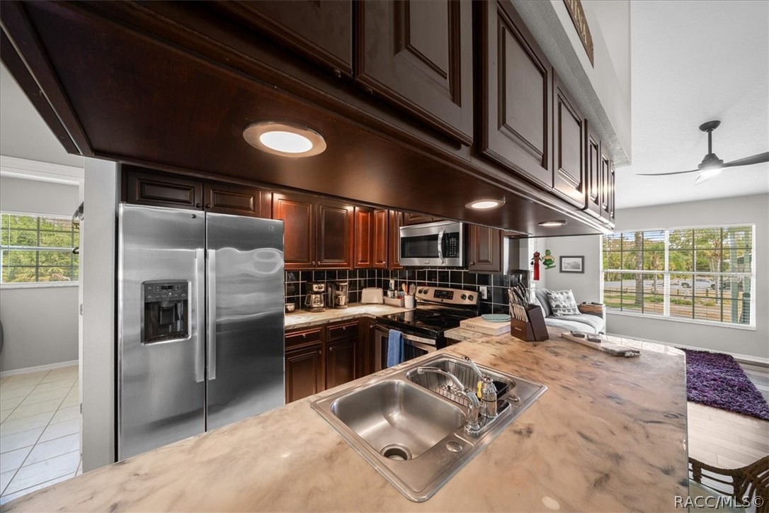 Kitchen with dark wood cabinetry, stainless steel appliances, and a large stone island with sink.