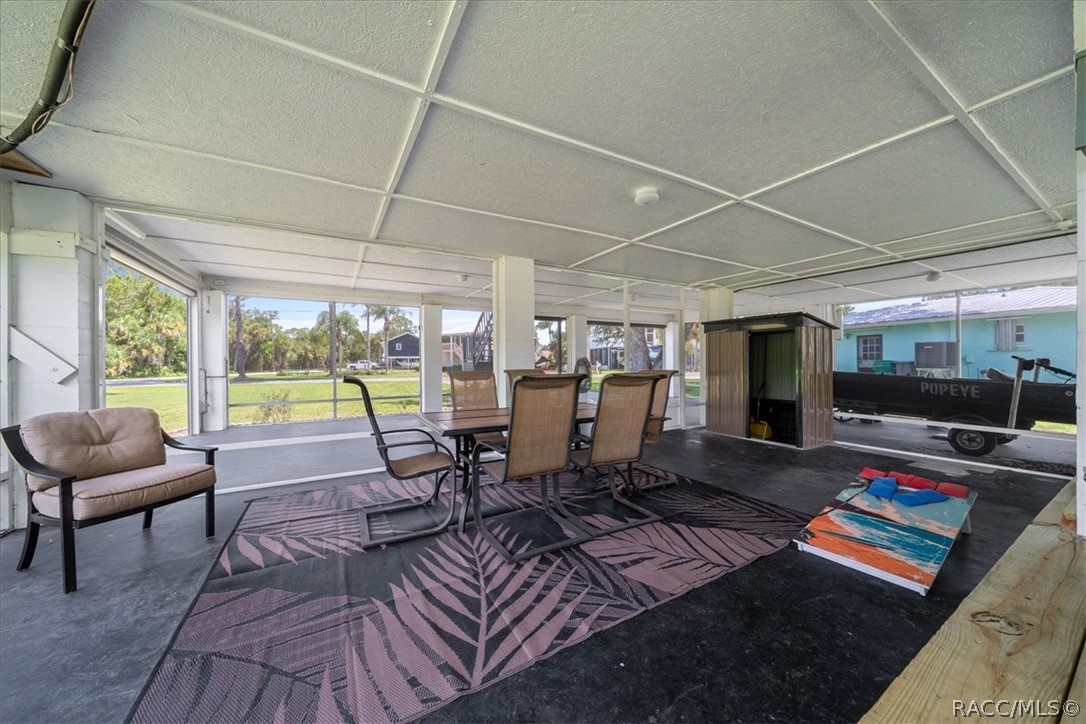 Screened-in patio with dining set, cushioned chair, patterned rug, and cornhole board.