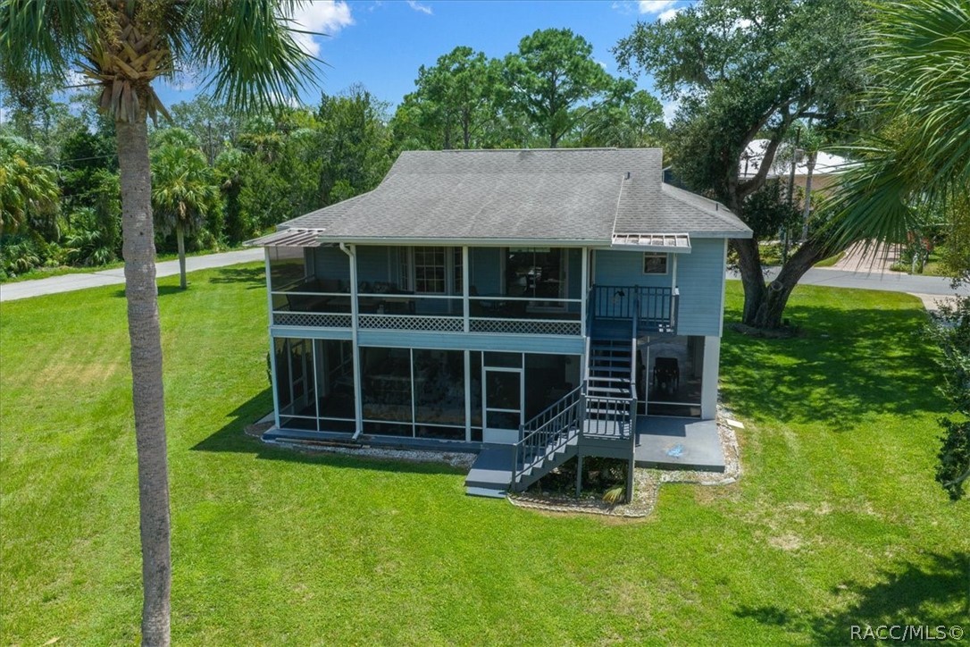 Rear of a blue two-story house with a screened patio, balcony, exterior stairs, and palm-lined lawn.