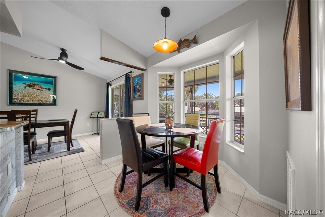 Dining area with round table, colorful chairs, tile floors, and large windows overlooking a covered patio.