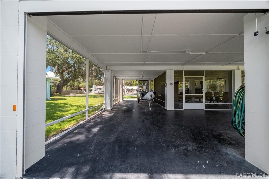 Covered carport with a boat on a trailer and sliding glass doors opening toward a grassy yard.