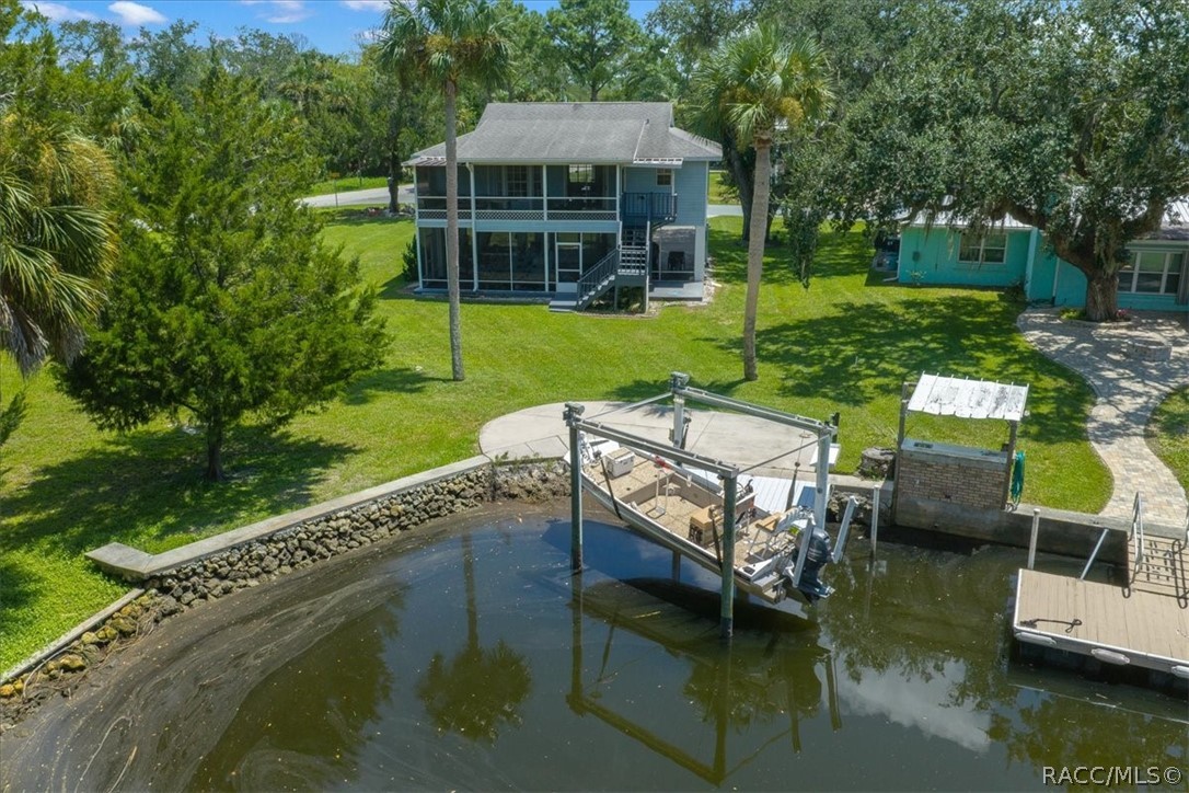 Aerial view of a two-story waterfront home and dock with boat lift along a canal.