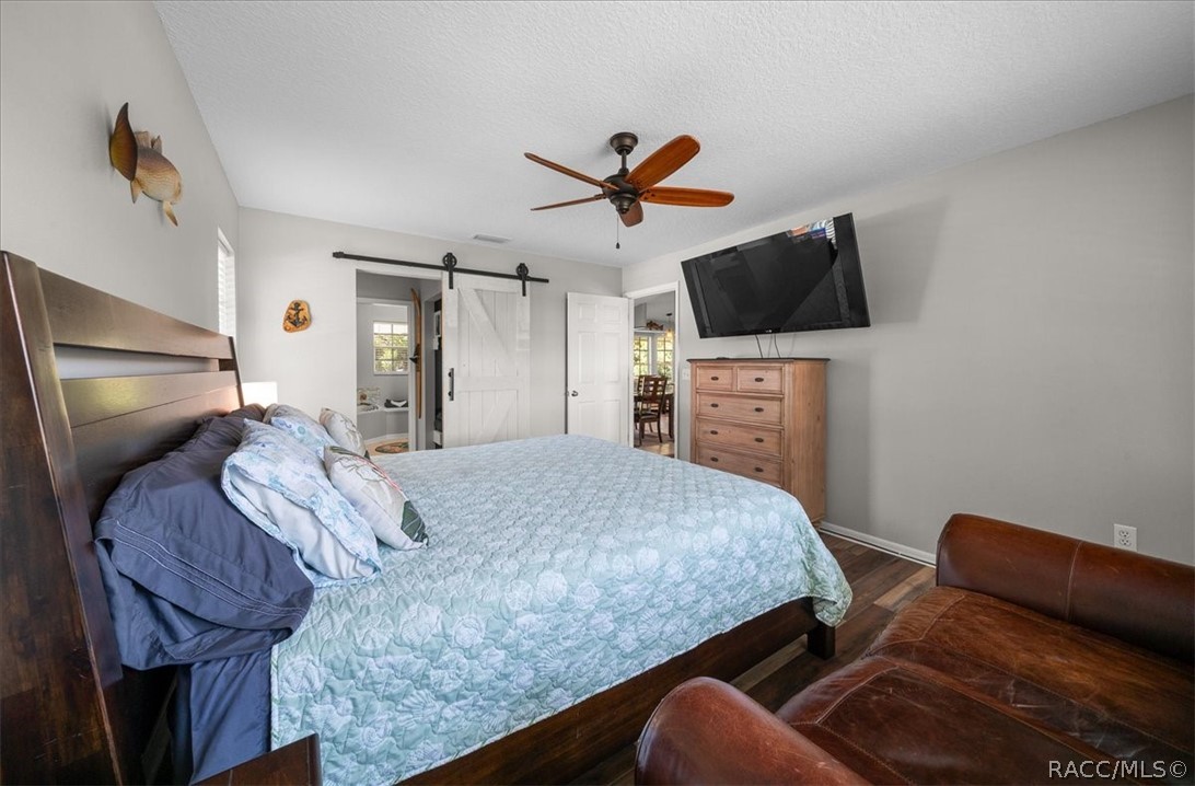 Bedroom with a pale blue quilt, dark wood bed, sliding barn door, and wall-mounted television.