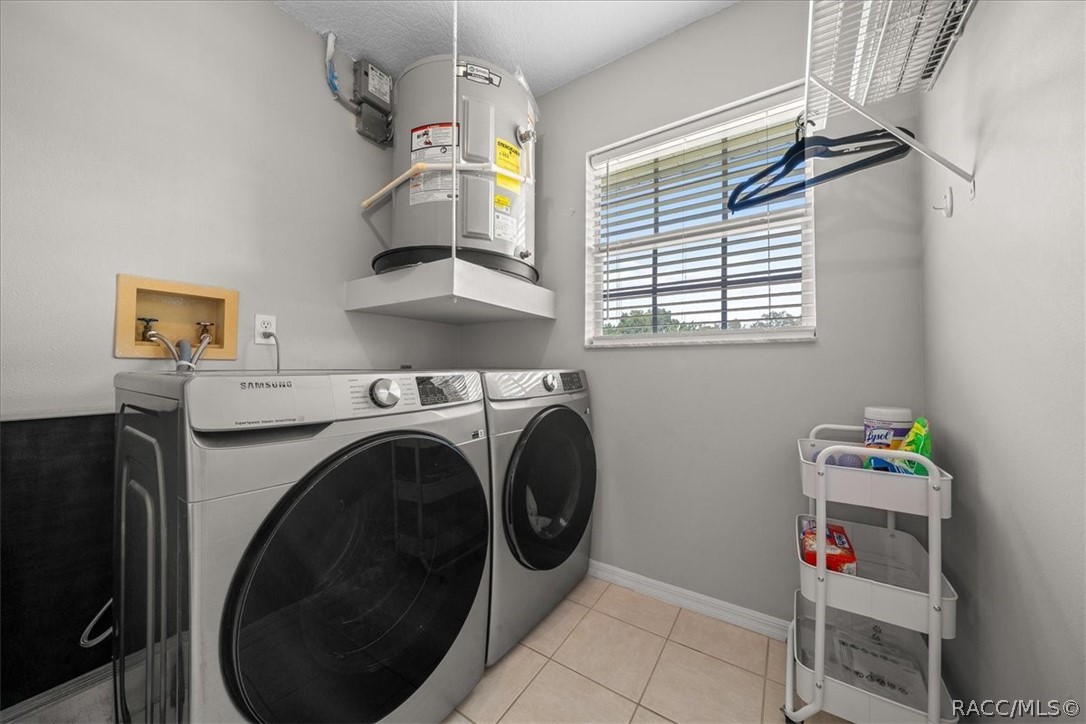 Laundry room with front-loading washer and dryer, elevated water heater, and window with blinds.