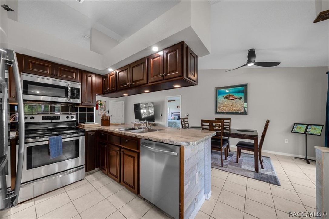 Kitchen with dark wood cabinets, a stone-topped island, and stainless steel appliances adjoining a dining area.