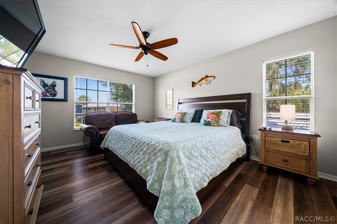 Furnished bedroom with a large bed, wood flooring, ceiling fan, and two windows.