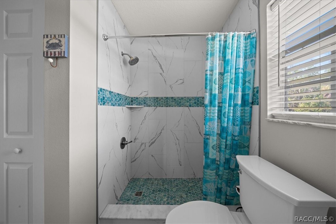 Bathroom with a marble-look walk-in shower, teal mosaic tile, and blue patterned curtain.