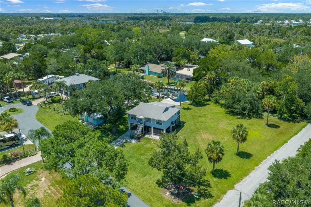Aerial view of a raised home on a spacious grassy lot among trees and neighboring houses.