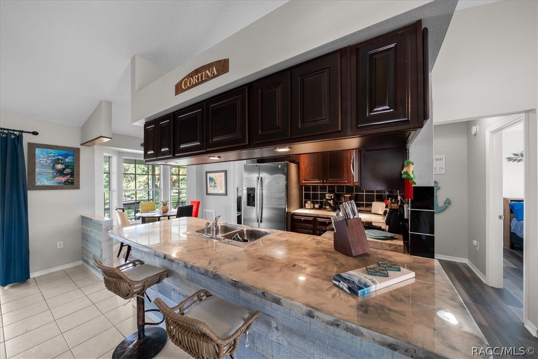 Kitchen with dark cherry cabinets, stainless steel appliances, and a large stone island with wicker bar stools.