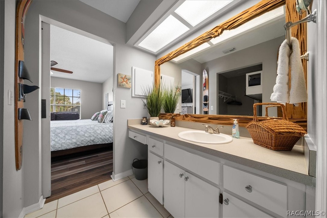 Bathroom vanity with a large wood-framed mirror and skylight, overlooking a bedroom through the open doorway.