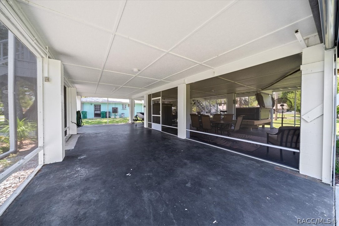 Covered patio with a dark concrete floor and screened walls overlooking a lawn.