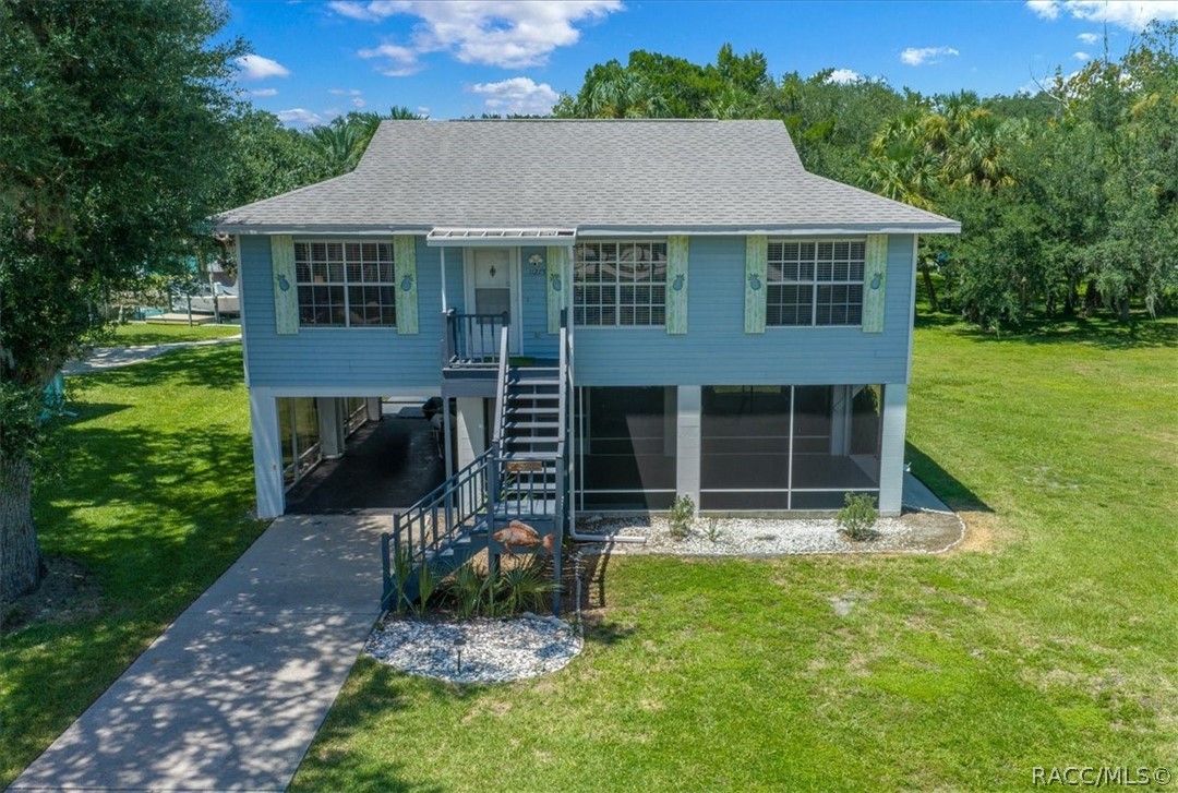 Raised blue house with pale green shutters, screened lower level, and front staircase.