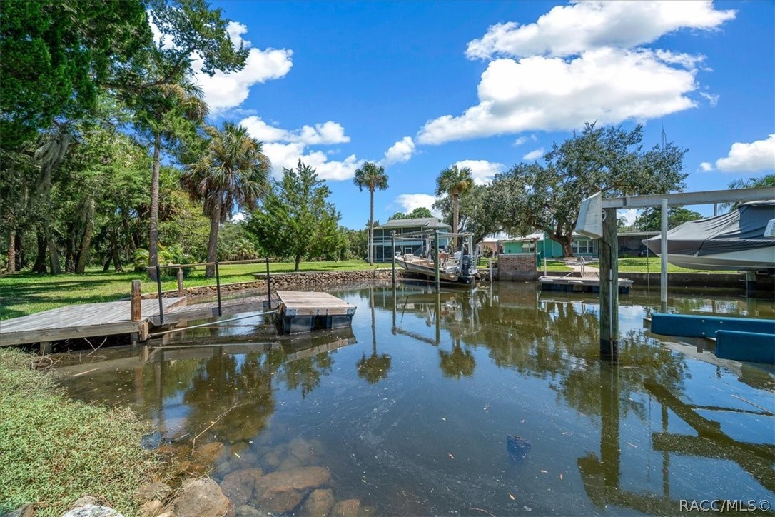 Canal waterfront with a wooden dock, boat lift, and covered boat beside a grassy yard.
