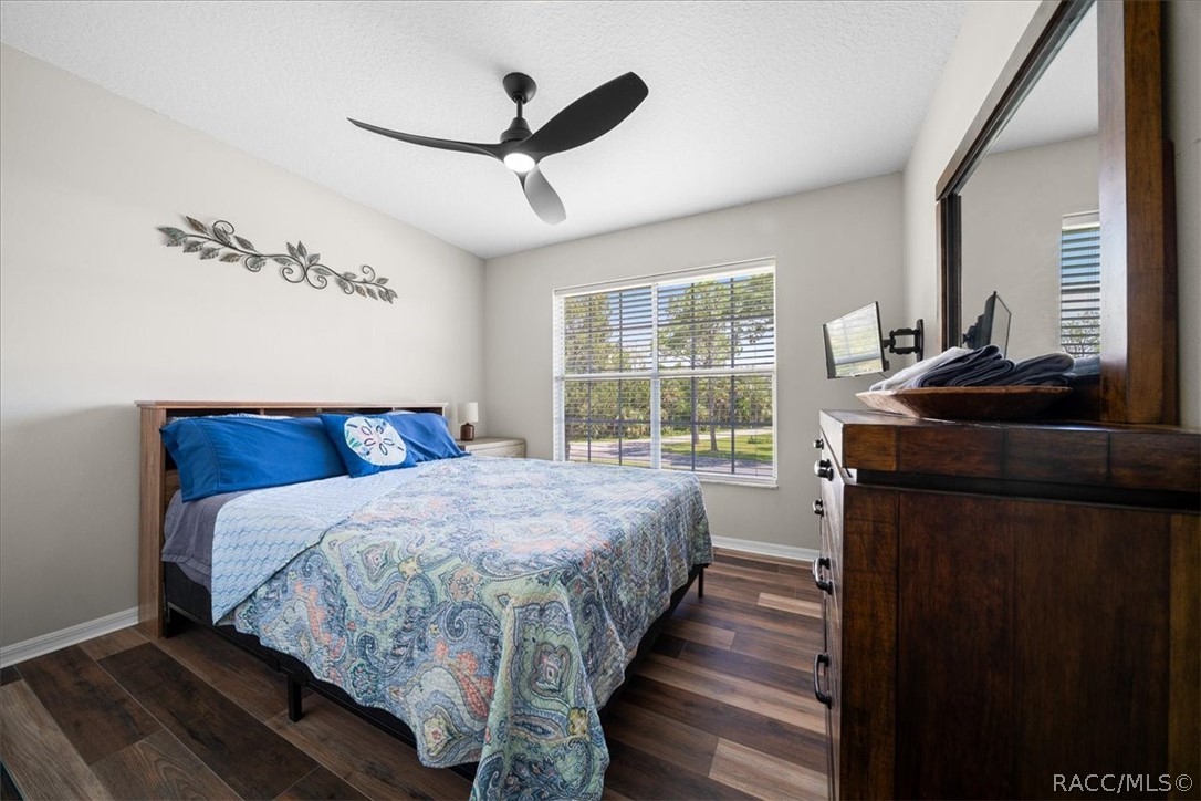 Furnished bedroom with a patterned quilt, dark wood dresser, and large window overlooking trees.