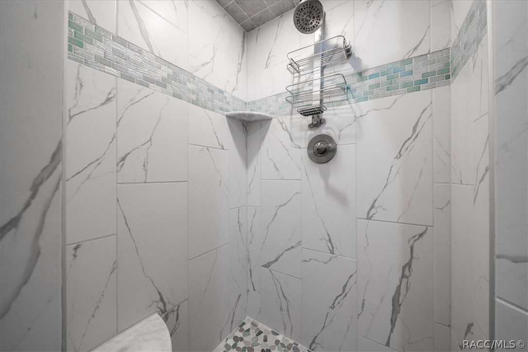 Walk-in shower with marble-look tile, a blue-green accent band, and a rainfall showerhead.