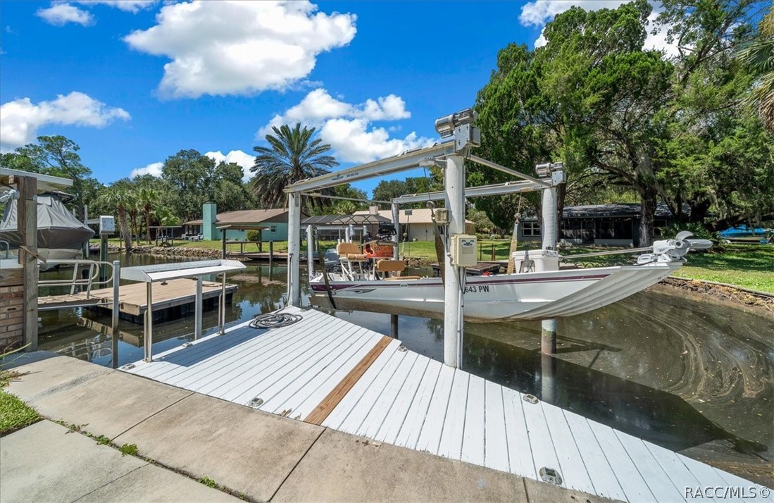 Canal-side dock with a white boat under a lift and neighboring waterfront homes.