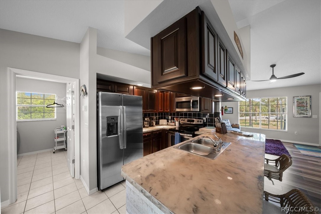 Kitchen with dark wood cabinets, stainless appliances, and a large stone island opening to a living area.