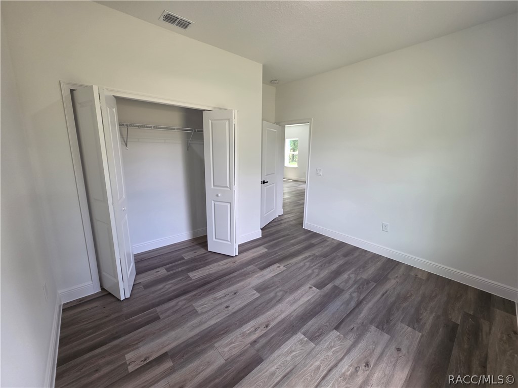 Empty bedroom with an open closet, white walls, and gray wood-look plank flooring.