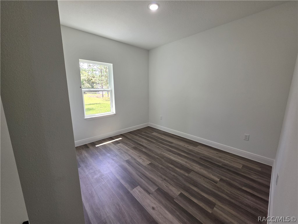 Vacant room with dark plank flooring, gray walls, and a window overlooking a grassy yard.